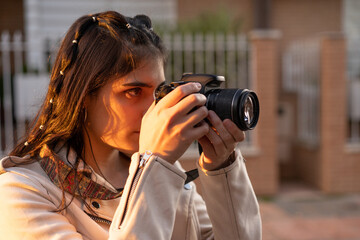 Joven mujer fotógrafa con una cámara réflex negra haciendo una foto al atardecer en un paisaje...