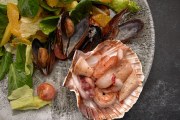 Seafood salad with pineapple and oranges on a plate, on a dark background