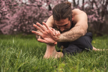 Young man stretching for a yoga session in the park. Fitness, healthy habits and wellness concepts.