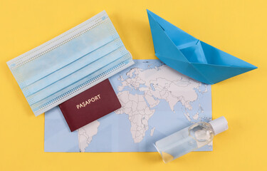 Passport and mask.
Passport with mask, disinfectant and paper boat with a map of the world on a yellow background, close-up top view.