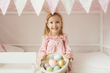  Little girl wearing bunny ears and holding a basket of Easter eggs. Happy Easter. Preparing family for Easter. Easter bunny ears.Smiling face