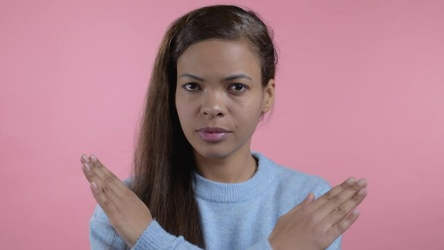 Mixed race woman disapproving with no crossing hands sign make basta, negation, enough gesture. Denying, Rejecting, Disagree, Portrait of pretty lady on pink background