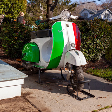 Clifton, VA, USA 11-14-2020: A Vespa scooter motorbike painted in the striped colors of Italian Flag (green, white and red) produced by Italian Piaggio motor company is parked in front of a house.