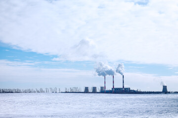 Fuming chimneys of factory on background of blue sky with clouds, and white snow