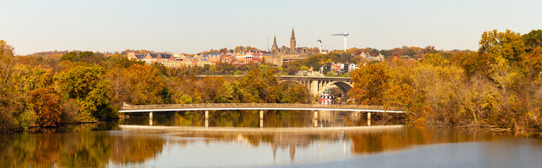 An autumn landscape panorama of Potomac river Theodore Roosevelt Island (left) and a small pedestrian bridge is seen. Francis Scott Key Memorial Bridge and Georgetown University is in the background. - obrazy, fototapety, plakaty