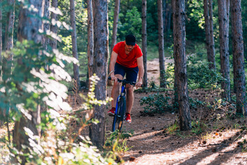 Fit cyclist riding his bike downhill through a forest ( woods ) while wearing a red shirt and red shoes.