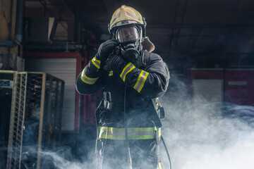 Portrait of a fireman wearing firefighter turnouts and helmet. Dark background with smoke and blue light.