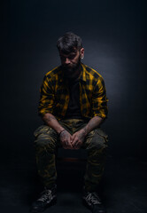 Fototapeta na wymiar Handsome male model with tattoos and tartan shirt is sitting on a chair isolated on a black background