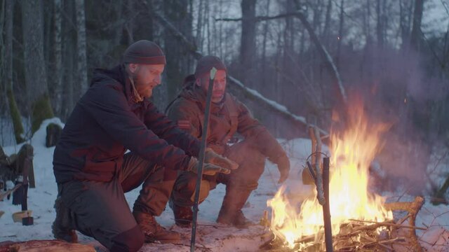 Two men near campfire in snowy forest