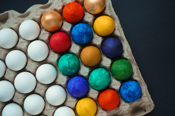 Lots of multiple colored and white eggs in a cardboard stand on a black background. Preparation for Easter, the concept of Easter. Top view