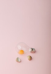 A raw egg in a light bulb and shells next to it. Easter 2021 minimal concept. Pink background.
