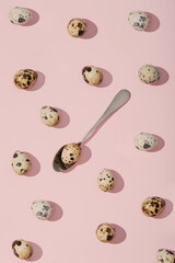 An irregularly arranged pattern consisting of quail eggs on a pink background with a spoon in the...