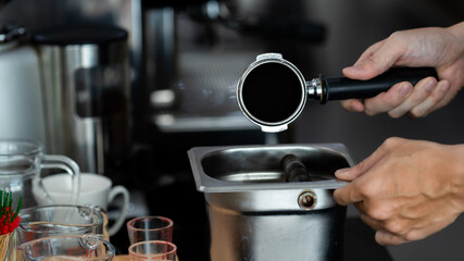 Close up hand. Ditching the coffee powder of male hands holding a metal tamper and a portafilter with coffee in a coffee shop. A man barista preparing for pressing ground coffee in cafe.