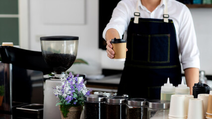 Asian young man smiling Holding paper coffee cup. At the bartender in the coffee shop. preparing for pressing ground coffee for brewing espresso or americano in a cafe. Concept Coffee maker in cafe.