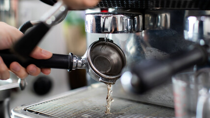 Fototapeta na wymiar Close up of warm water rinsing at the pouring from coffee machine. A man barista preparing for pressing ground coffee for brewing espresso or americano in a cafe.