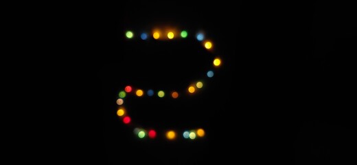 Closeup of Number (2) made with multicolored blurred bokeh Christmas lights in a isolated black background with copy space