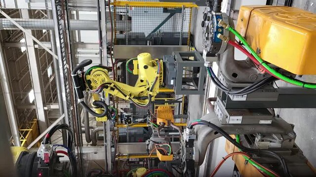 vertical panning shot of a yellow spot welding robot with green tires and wires in a bright industrial building