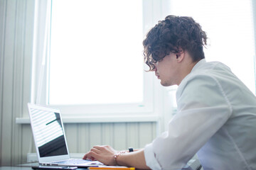 Caucasian man with curly hair working at the laptop. against the background of the window. side view.