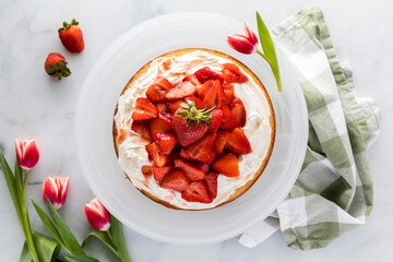 Top down view of a whole strawberry shortcake surrounded by tulips and strawberries. A spring food concept.