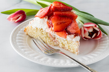 Close up of a slice of strawberry shortcake on a white plate ready for eating.