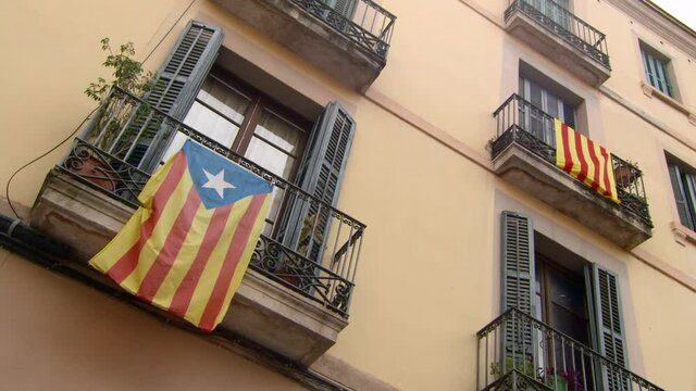 Flag Of Catalonia And Estelada Blava Hang From Different Wrought Iron Balconies In Sunshine On Limestone Fa�ade