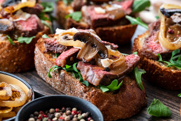 Close up of a toasted steak sandwich topped with sauteed mushrooms and caramelized onions, ready for eating.