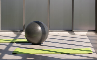 Gray color fit ball exercise is equipment for healthy put on green carpet indoor on morning day with sunlight and copy space for a graphic designer
