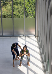 Top view adult asian women in exercise suit do squat fitness bend the knees intend and determination with trainer coach near a window in the morning with sunlight