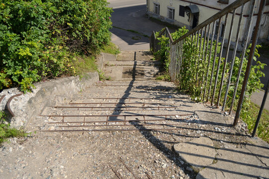Image of crumbling old concrete stone steps of a staircase with metal railings descending down to a street overlooking an ancient building