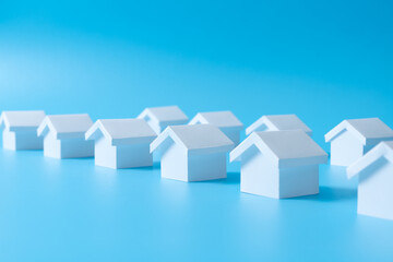 Fototapeta na wymiar Row of miniature 3D white houses on blue background for real estate property, housing development or community