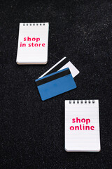 shop in store vs shop online texts on notepads with payment cards next to them, competition and retail industry