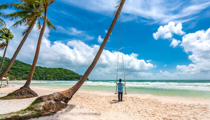 Silhouette of traveler man sitting on a swing beside coconut trees watching the paradise beach on Phu Quoc island, Vietnam
