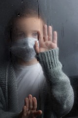 A young boy stands at the window with a raindrop on the glass after the rain.