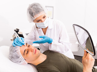 Naklejka premium Confident woman cosmetologist examining male client face before procedure in esthetic clinic