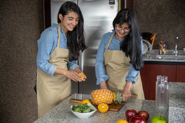Madre e hija mexicanas  cortando frutas en la cocina y riendo, día de la familia y día de la madre
