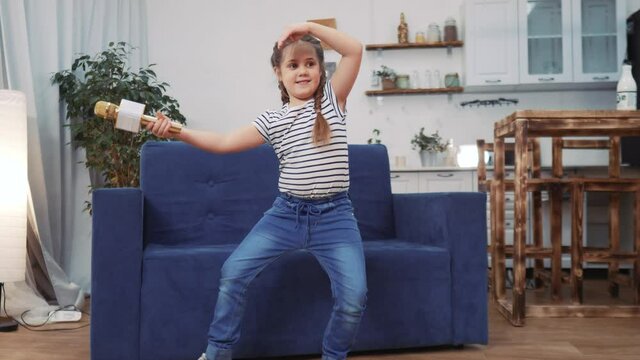 little child daughter a sing dancing at home. stay home active leisure happy childhood concept. child daughter dancing sing next to the sofa with a microphone dream. kid dance dream