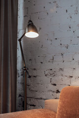 Golden floor lamp and orange comfortable sofa in an elegant living room interior with an old brick wall
