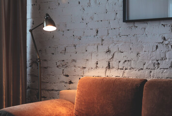 Golden floor lamp and orange comfortable sofa in an elegant living room interior with an old brick...
