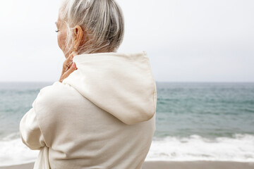 Senior woman in hoodie relaxing at the beach - Powered by Adobe