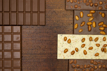 a lot of different types of chocolate lie on a brown background with nuts and chocolate flakes