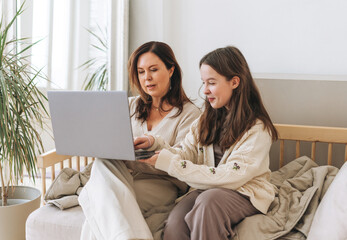Mother middle aged woman and daughter teenager using laptop together in the light interior