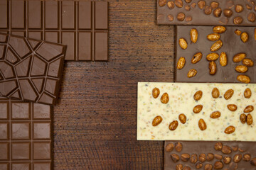 a lot of different types of chocolate lie on a brown background with nuts and chocolate flakes