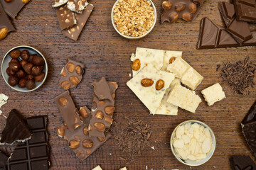 a lot of different types of chocolate lie on a brown background with nuts and chocolate flakes