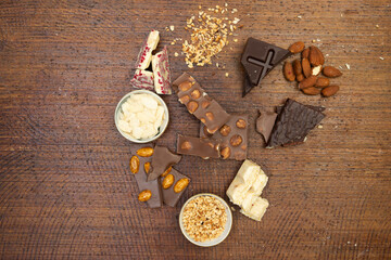 a lot of different types of chocolate lie on a brown background with nuts and chocolate flakes