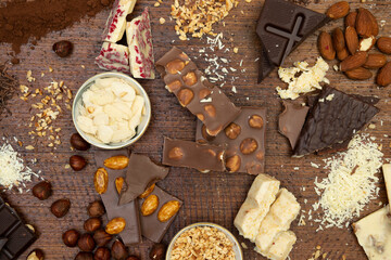 a lot of different types of chocolate lie on a brown background with nuts and chocolate flakes