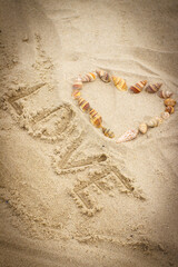 Word love written on sand at beach, heart of shells