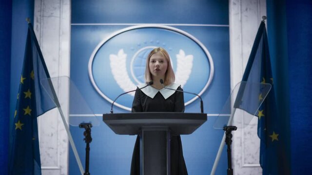 Young Girl Activist Delivering an Emotional and Powerful Speech at Press Conference in Government Building. Child Speaking to Congress at Summit Meeting. Backdrop with European Union Flags.