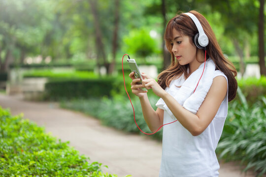 Image of young Asian woman wearing headphone outdoor exercise in park.