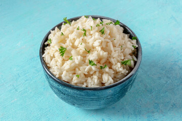 A bowl of white rice with parsley leaves, on a blue background