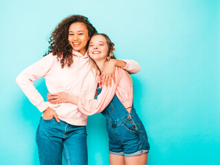 Two young beautiful smiling international hipster female in trendy summer clothes. Sexy carefree women posing near blue wall in studio. Positive models having fun in sunglasses. Concept of friendship